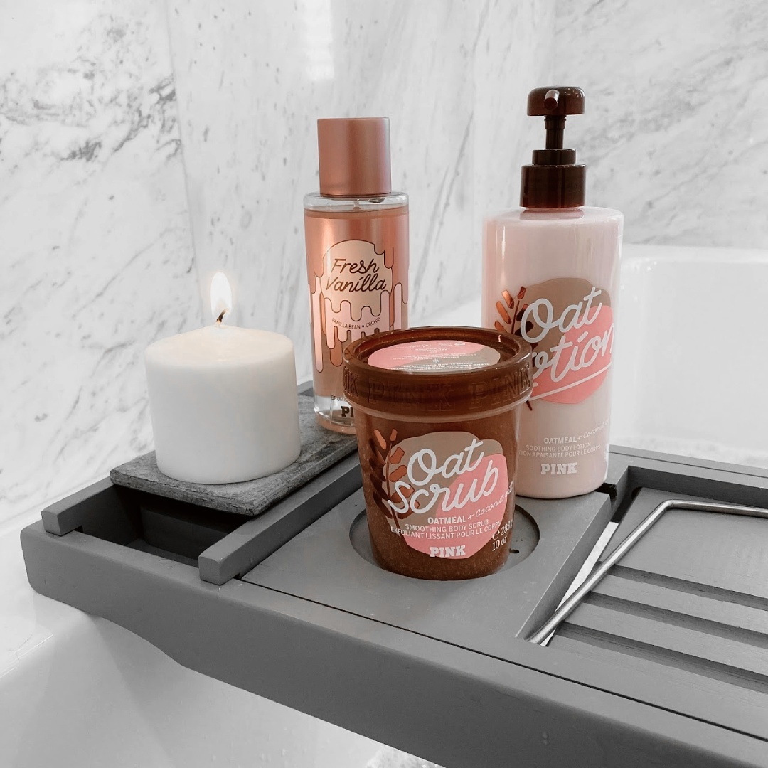 Product array of PINK beauty products with a candle on a bathtub tray.